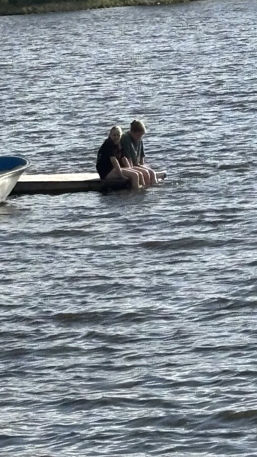 Zwei Personen sitzen mit den Füßen im Wasser an einem See
