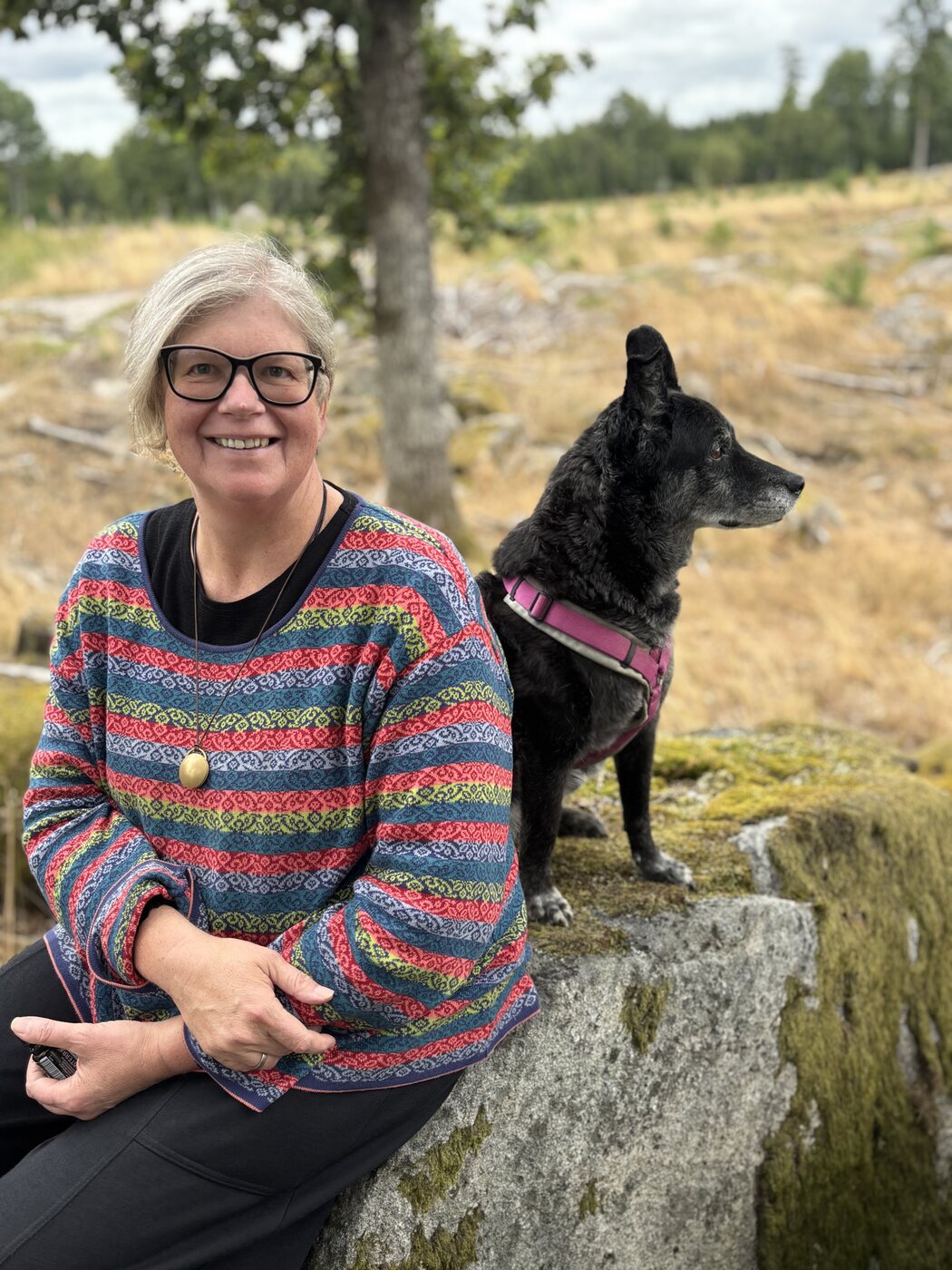 Nicola sitzt lächelnd neben Hündin Lucy auf einem großen Stein in Schweden