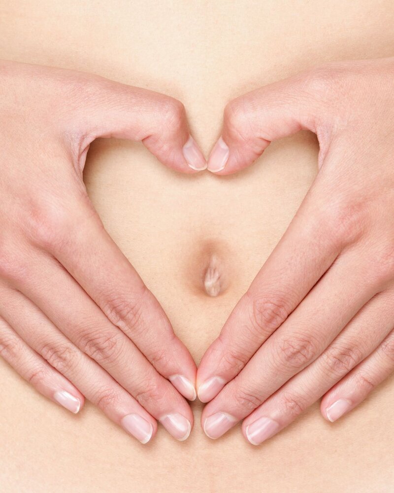 Hände formen ein Herz über dem Bauch